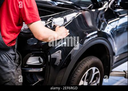 Nahaufnahme der Auto-Mechaniker Hände in Coverall auf schönen schwarzen Auto für die Überprüfung Auto bei der Service. Selektiver Fokus Stockfoto