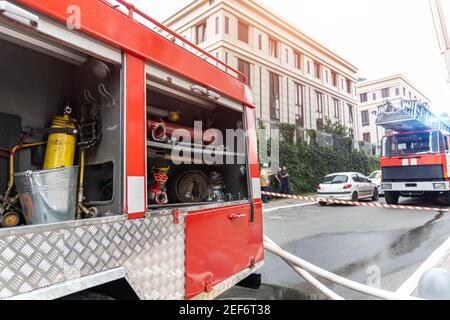 Feuerwehrmänner tragen Uniform hinter Feuerband und viele Feuer stehen Motorfahrzeuge mit Leiter bei Unfall im Hochhaus Wohngebäude Oder Bürogebäude Stockfoto