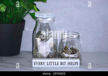 Text auf Holzblock mit australischen und europäischen Münzen auf Tischfläche mit Pflanzenhintergrund - jede kleine Spitze hepls. Wohltätigkeitskonzept Stockfoto