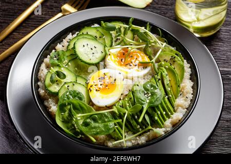 Quinoa Schüssel mit Ei, Sonnenblumen-Mikrogemüse, Gurke, Avocado, Baby Spinat in einer schwarzen Schüssel auf einem dunklen Holztisch, türkische Küche Stockfoto