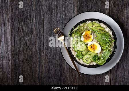 Quinoa Schüssel mit Ei, Sonnenblumen-Mikrogemüse, Gurke, Avocado, Baby Spinat in einer schwarzen Schüssel auf einem dunklen Holztisch, türkische Küche, flat lay, Stockfoto