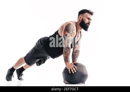 Muskulös tätowiert bärtig männlich Ausübung Fitness Gewichte Medizin Ball Liegestütze Übungen im Studio isoliert auf weißem Hintergrund. Stockfoto