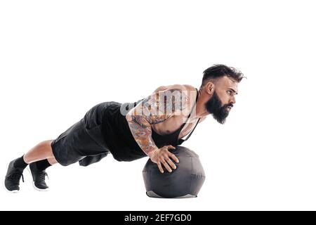 Muskulös tätowiert bärtig männlich Ausübung Fitness Gewichte Medizin Ball Liegestütze Übungen im Studio isoliert auf weißem Hintergrund. Stockfoto