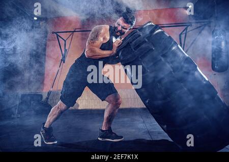 Bodybuilding-Training, bärtige starke Sportler mit muskulösen Körper heben schwere Rad in der Turnhalle. Stockfoto