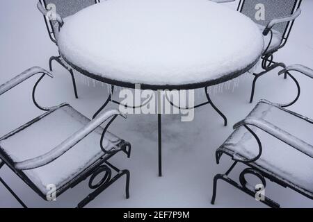 Gefrorener und schneebedeckter Tisch und Stühle im Freien nach Schnee und eiskalten Regen im Winter. Stockfoto
