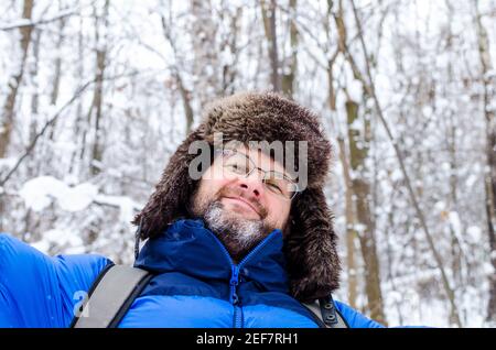 Ein Mann mittleren Alters in Pelzmütze und Brillen genießt in Der Winterwald Stockfoto