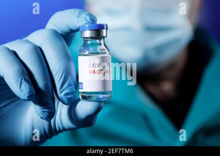 Arzt mit medizinischen Kappen und Latexhandschuhen nimmt die auf Covid Impfstoff mit einer Spritze in einem Tisch mit mehreren Fläschchen Stockfoto