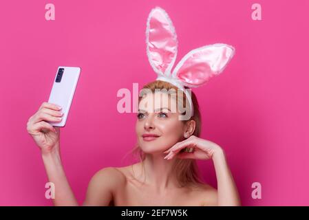 Junge Frau mit Hasenohren. Blogger halten Telefon isoliert rosa. Stockfoto