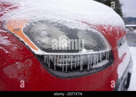 Nahaufnahme des Scheinwerfers eines gefrorenen Autos auf den Straßen nach einem Wintersturm von Schnee und eiskalten Regen. Stockfoto