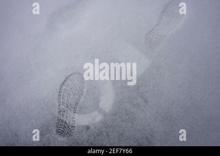 Fußabdrücke, bemalte Parkplatznummermarkierungen und eine dünne Schneeschicht auf dem Boden außerhalb der Garage. Stockfoto