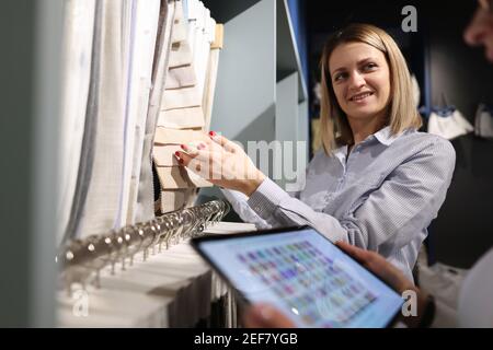 Frau wählt Farbe des Stoffes im Salon neben Berater Mit Tablet Stockfoto