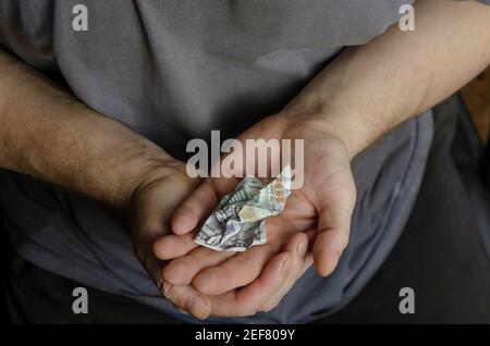 Zerknittertes Geld liegt in offenen Handflächen. Ein erwachsener Mann hält einen faltigen Hundert-Dollar-Schein in seinen Händen. Blick von oben aus einem Winkel. Selektiver Fokus Stockfoto