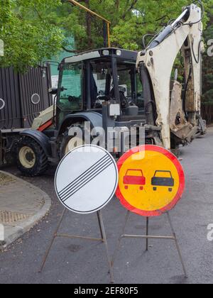 Runde Straßenschilder stehen auf der Straße mit Bagger im Hintergrund. Reparaturarbeiten auf der Straße Stockfoto