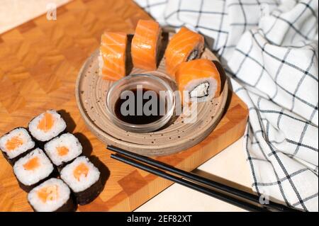 Japanische Sushi-Brötchen auf dem Teller mit Holzhintergrund. Sushi-Brötchen Philadelphia, Maki, Essstäbchen und Sojasauce Stockfoto