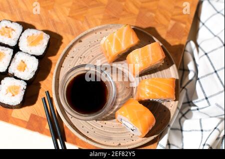 Japanische Sushi-Brötchen auf dem Teller mit Holzhintergrund. Sushi-Brötchen Philadelphia, Maki, Essstäbchen und Sojasauce Stockfoto