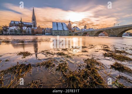Sonnenuntergang bei Donauüberflutung im Winter 2021 in Regensburg mit Blick auf den Dom, die Altstadt und die überflutete Promenade und die Steinbrücke, Germa Stockfoto