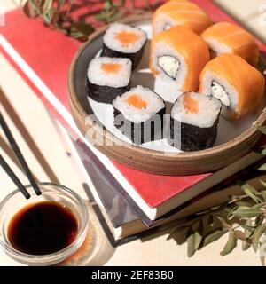 Japanische Sushi-Brötchen auf hellem Teller mit beigefarbenem Hintergrund. Buch und Mittagessen. Home Relax Konzept. Gemütliche Stimmung Stockfoto
