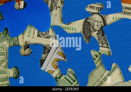 Unter den Puzzleteilen sind amerikanische Dollar verschiedener Konfessionen versteckt. Blaue Rätsel. Draufsicht, Flat Lay. Stockfoto
