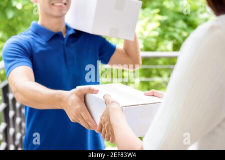 Lächelnder Lieferer in blauer Uniform, der Paketkasten anliefert Eine Frau - Kurier-Service-Konzept Stockfoto