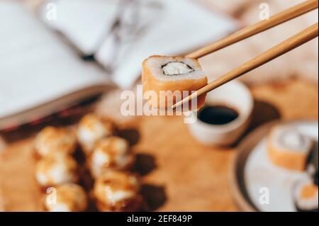 Japanische Sushi-Rollen mit schwarzen Essstäbchen. Sushi-Brötchen mit Sahne, Maki, Essstäbchen und Sojasauce Stockfoto