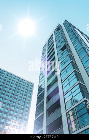 Mehrstöckige Gebäude mit einer Glasfassade und im Bau mit einer Fassadenabteilung, mit einer hellen Sonne am Himmel Stockfoto