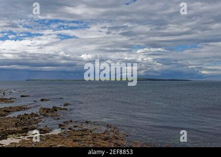 Blick auf die Insel Stroma, Teil der Orkneys, vom felsigen Strand von John OÕGroats an einem schönen späten Nachmittag im Mai. Stockfoto