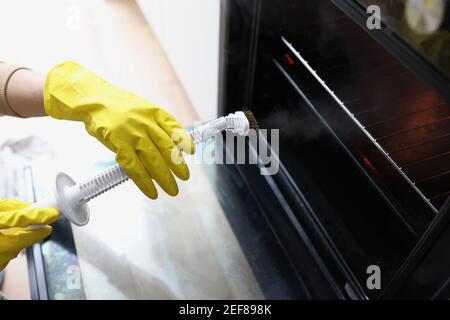 Weibliche Hände in gelben Handschuhen halten einen Dampfreiniger Und Reinigungsofen Stockfoto