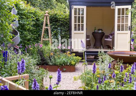 Ein kleiner englischer Cottage-Garten mit Summerhouse Shepherds Hut in Kiesgarten - Arbeit vom Home Office - Hochbeet Blume Border Obelisk - Großbritannien Stockfoto