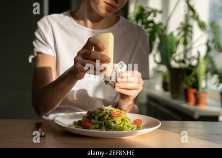 Nahaufnahme der Frau Hände Reibe Parmesan Käse in Pasta mit Sauce Pesto, frische Kirschtomaten. Stockfoto