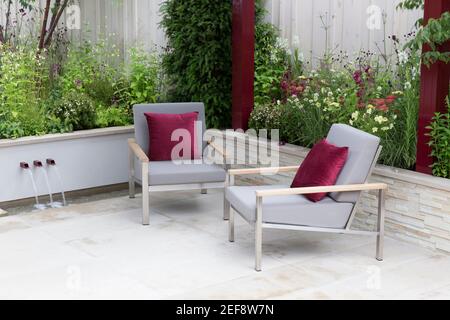 Moderne urbane Steingarten Terrasse mit Gartenmöbeln Stühle mit roten Kissen - Hochbetten Garten Blumengrenze - Sommer - London UK England Stockfoto