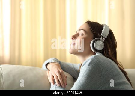 Profil einer Frau, die atmet und Musik mit Kopfhörern hört Auf einer Couch zu Hause Stockfoto