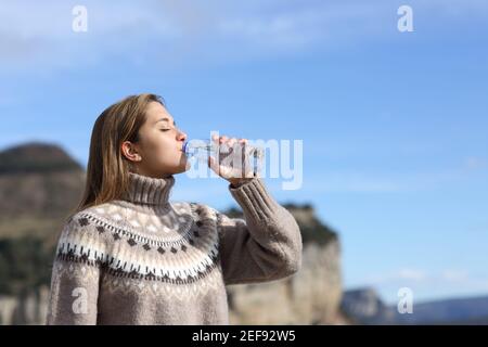 Seitenansicht Porträt einer Frau, die Wasser aus Kunststoff trinkt Flasche im Winter in den Bergen Stockfoto