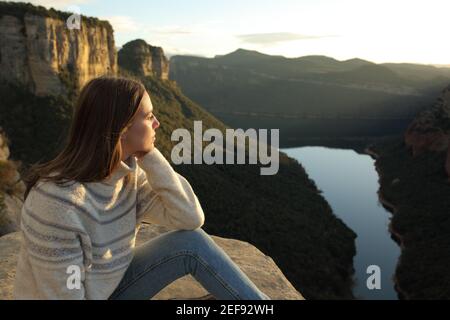 Nachdenkliche Frau, die die Aussicht auf der Spitze einer Klippe betrachtet In den Bergen bei Sonnenuntergang im Winter Stockfoto