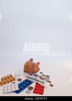 Sparschwein mit Geld, Pillen, Medikamenten, Spritze, Ampullen auf weißem Hintergrund. Behandlungskosten. Gewinne bei Arzneimitteln. Stockfoto