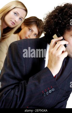 Geschäftsmann, der mit seinen beiden Sekretärinnen auf einem Mobiltelefon spricht Hinter ihm stehen Stockfoto