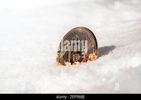 Bitcoin liegt auf dem Schnee und funkelt in der Sonne. Stockfoto