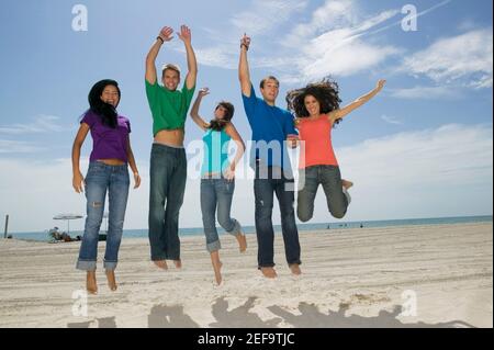 Low-Angle-Ansicht von drei jungen Frauen und zwei jungen Männer springen am Strand Stockfoto