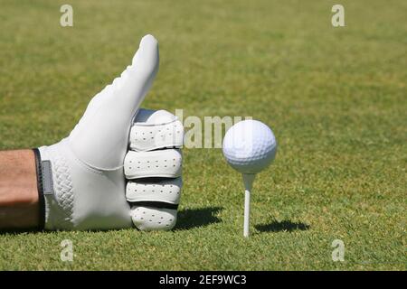 Nahaufnahme einer personÅ½s Hand, die ein Daumen hoch Zeichen macht Neben einem Golfball auf einem Abschlag Stockfoto