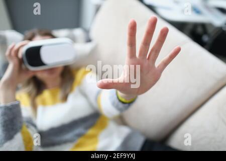 Frau in Virtual-Reality-Brille liegt auf der Couch und hält Die Hand nach oben Stockfoto
