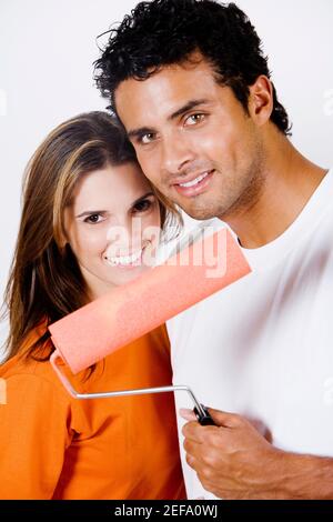 Porträt eines jungen Mannes, der eine Malrolle im Stehen hält Mit einer mittleren erwachsenen Frau Stockfoto