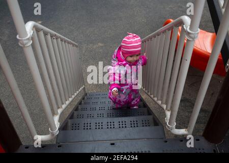 Kleines Kleinkind in warmen Winteroveralls spielt auf dem Spielplatz. Weicher Fokus Stockfoto