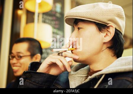 Seitenprofil eines mittleren Erwachsenen, der eine Zigarette raucht Und ein junger Mann lächelte neben ihm Stockfoto