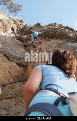 Low-Angle-Ansicht einer weiblichen Kletterer Blick auf Ein männlicher Bergsteiger, der eine Felswand bestieckt Stockfoto