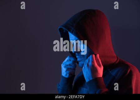 Ein mit farbigen Neonlichtern beleuchteter Mann setzt ein hoodie Stockfoto