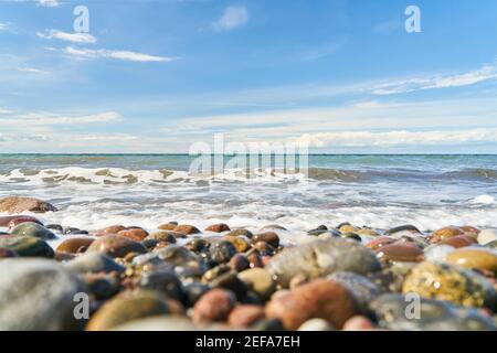 Kieselsteine am Strand am Meer mit Wellen und Himmel mit Wolken Stockfoto