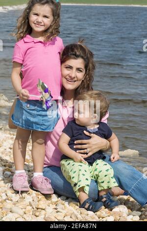 Portrait einer mittleren erwachsenen Frau auf Steinen sitzend mit Ihre beiden Kinder am waterÅ½s-Rand Stockfoto