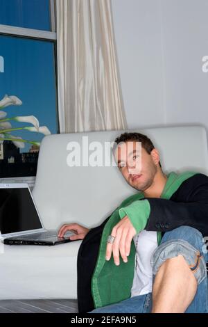 Porträt eines jungen Mannes, der sich an eine Couch lehnt und Arbeiten auf einem Laptop Stockfoto