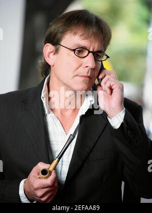 Nahaufnahme eines reifen Mannes, der eine Pfeife hält und spricht Auf einem Mobiltelefon Stockfoto