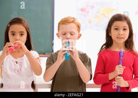 Schuljunge mit zwei Schülerinnen spielen Flöten in einem Klassenzimmer Stockfoto