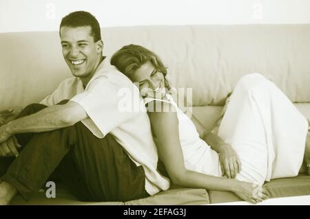 Seitenprofil eines jungen Paares, das sich von hinten nach hinten zurücklehnen kann Auf der Couch und lächelnd Stockfoto